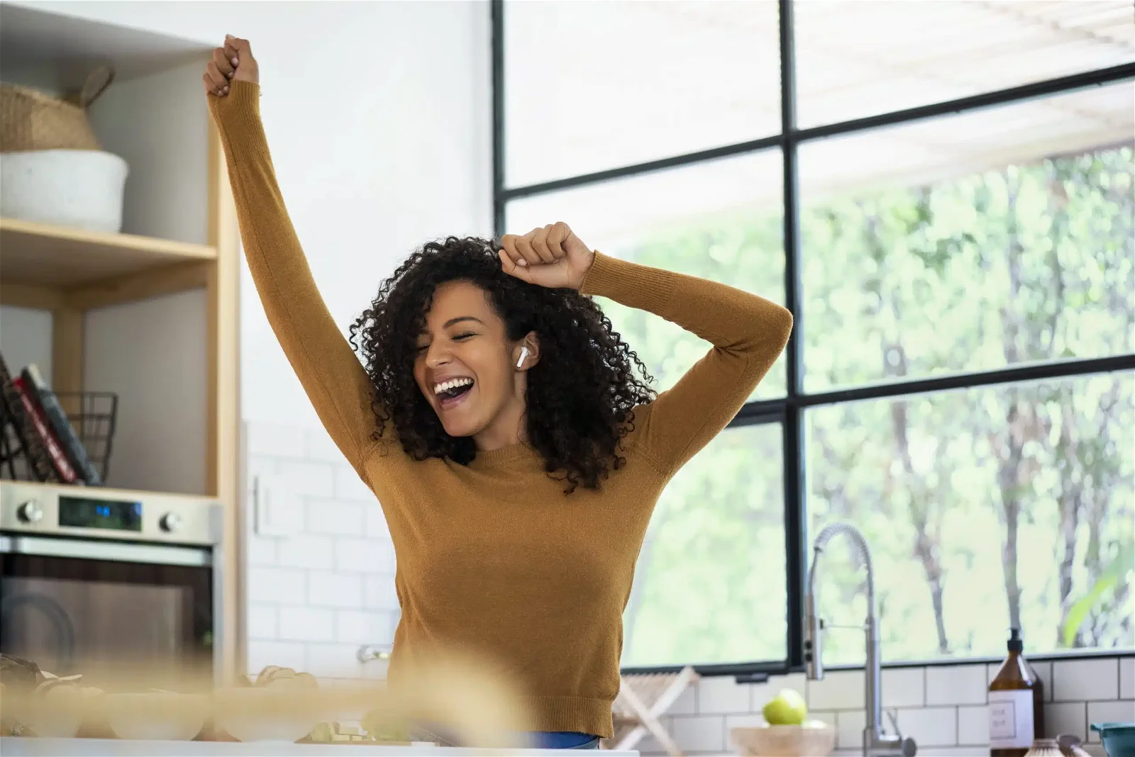 Smiling woman listening music and dancing in kitchen