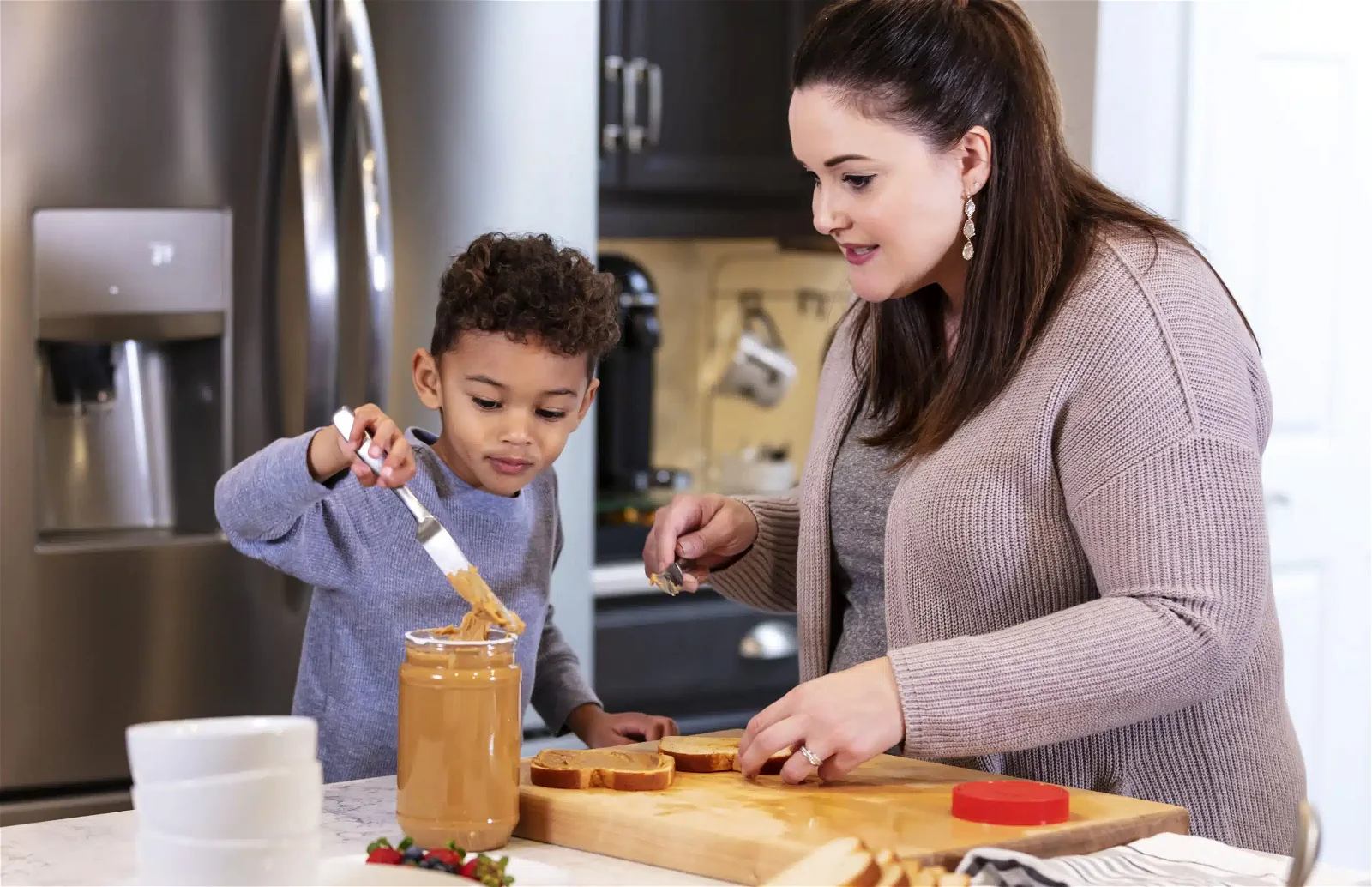 Multi-ethnic mother, son making peanut butter sandwiches