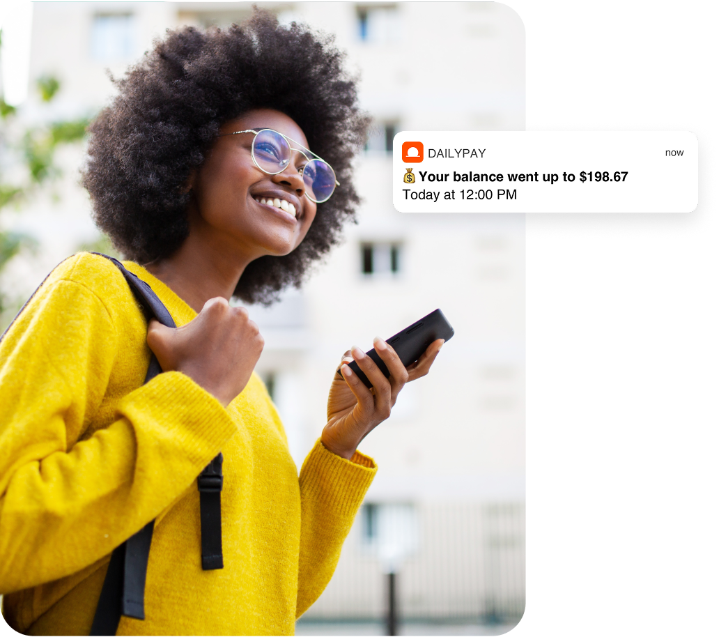 A person outdoors smiles while holding a phone. A notification on the screen reads, “Your balance went up to $198.67. Today at 12:00 PM.”.